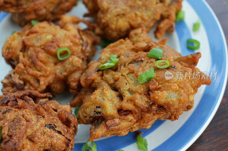 近距离拍摄自制的脆洋葱bhajis / pakoras配以切碎的葱，放在蓝色和白色的康沃尔餐具盘上，印度菜素食小吃，高架视野，聚焦前景